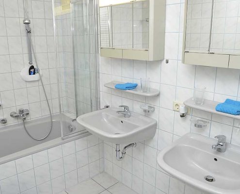 Badezimmer 2 mit Badewanne, Duschwand, zwei Waschbecken mit Spiegelschränken - und im Vorraum ein WC mit zusätzlichem Waschbecken.